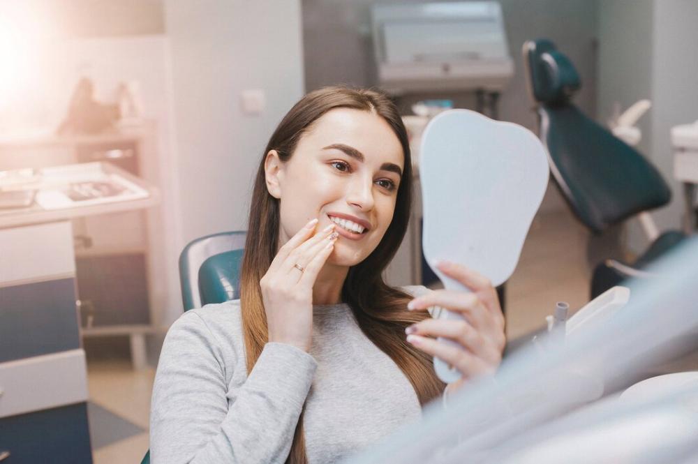 A lady smiling at a mirror after tooth-colored fillings in Alpharetta Creek Restorative Dentistry