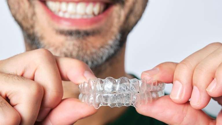 A man smiling while holding a clear aligner in Alpharetta