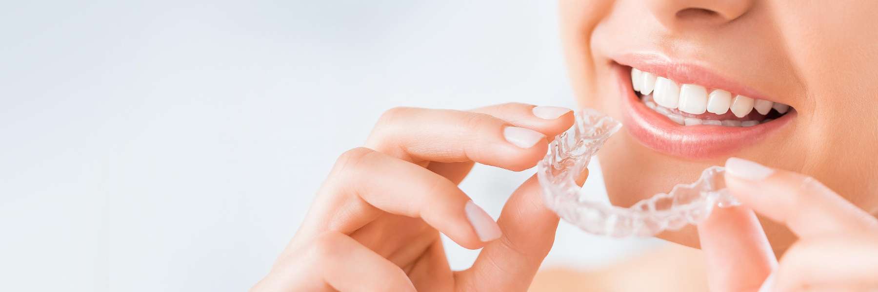 A woman smiling while holding a clear aligner in Alpharetta
